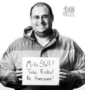 Professor Joey Lopez holding a sign that says "Make stuff! Take risks! Be awesome!"
