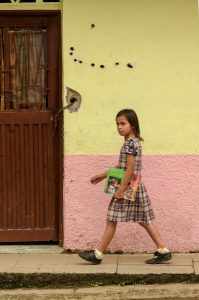 Young school girl walking home past bullet holes in wall