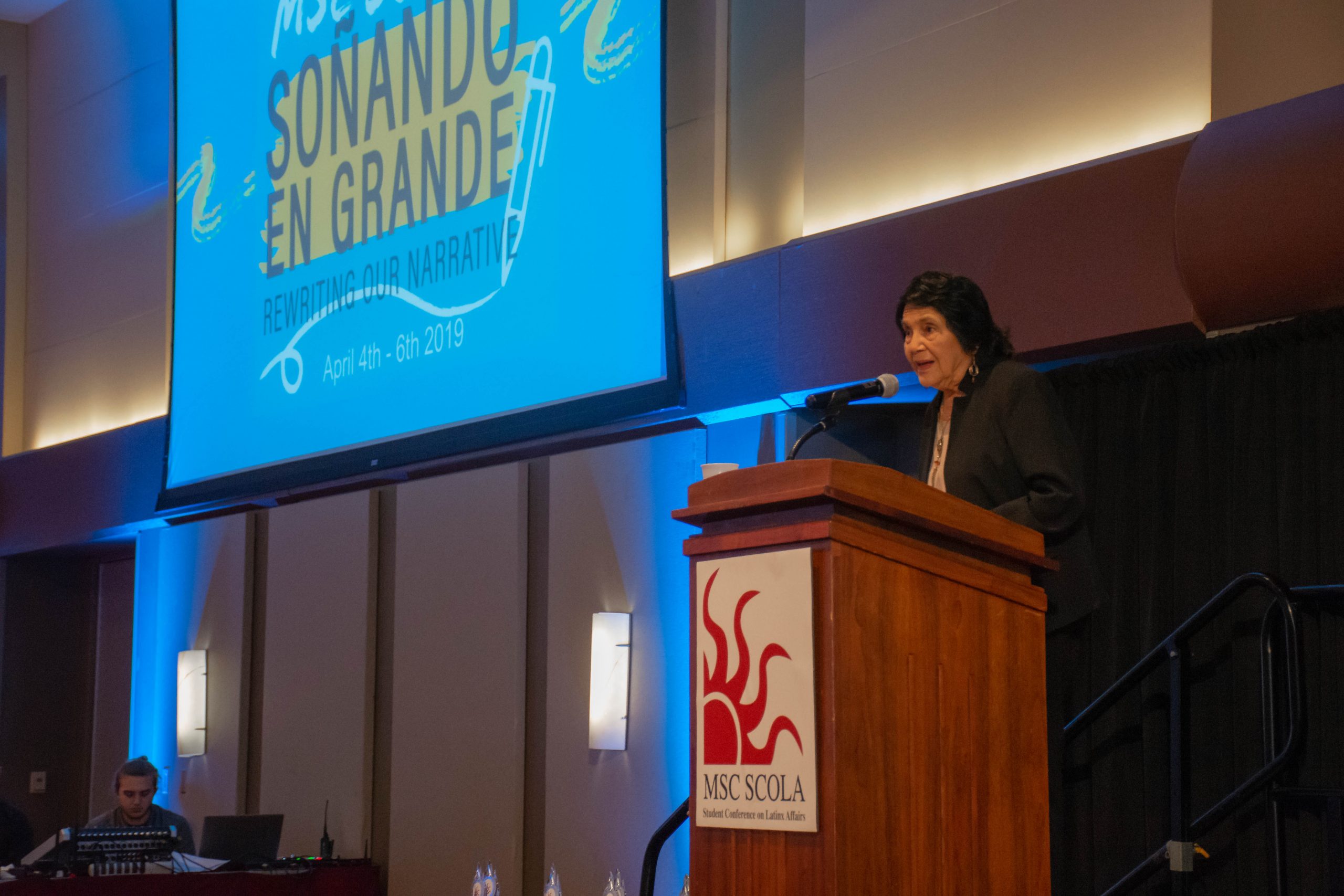 Dolores Huerta speaking behind a podium at MSC SCOLA 2019