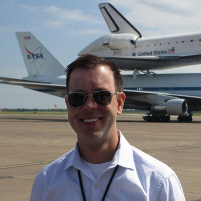 Josh Byerly '99 on the tarmac with the Space Shuttle Endeavour atop a NASA Shuttle Carrier Aircraft in the background.