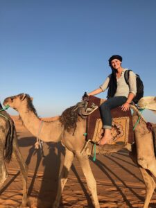 Barefoot student rides camel through Sahara Desert during summer study abroad program in Morocco.