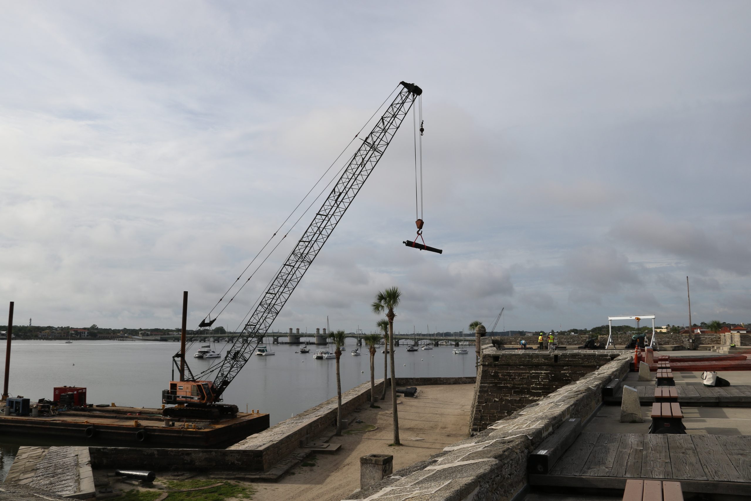 crane lifting cannon onto a barge alonside the fort