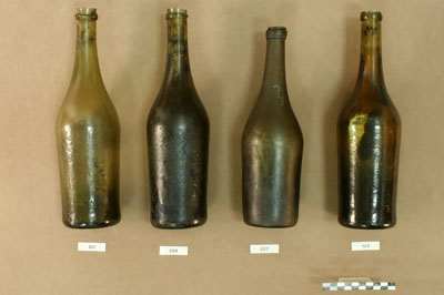 The wine bottles are characterized by sloping shoulders and were most likely cast using the dip-mold technique of bottle manufacturing.