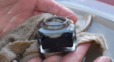 Glass inkwell on damp cloth on hands over water. The inkwell still contains traces of ink.