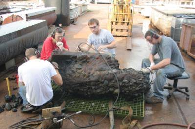 Texas A&M Graduate students using ball-pee hammers, chisels, and air scribes to carefully remove the concretion, exposing the iron carronade and wooden carriage beneath.