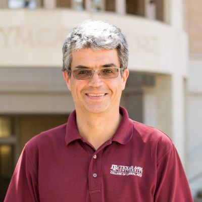 Professor Jose Luis Bermudez standing in a shaded area outside the YMCA building on Texas A&M's campus