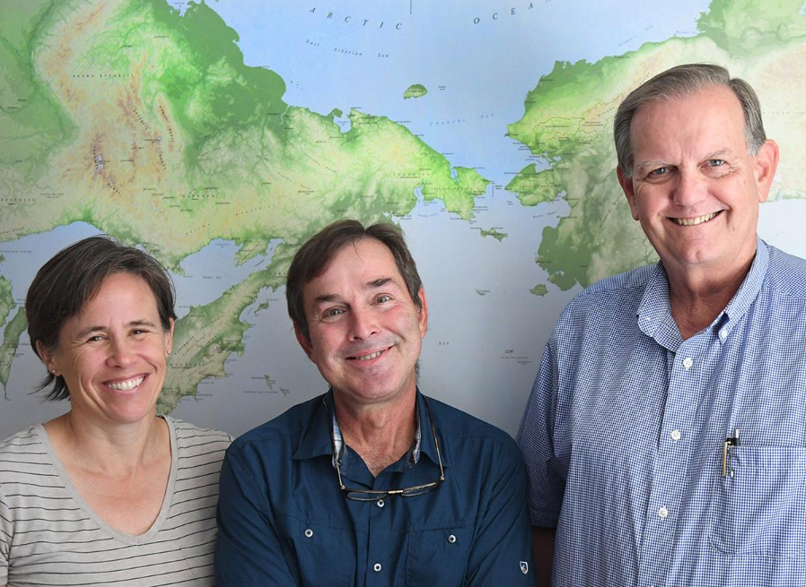 Kelly Graf, from left, Ted Goebel and Michael Waters of the Center for the Study of the First Americans, stand in front of a map showing where modern man is believed to have crossed over from present-day Siberia to North America while standing in their offices at the anthropology building at Texas A&M.