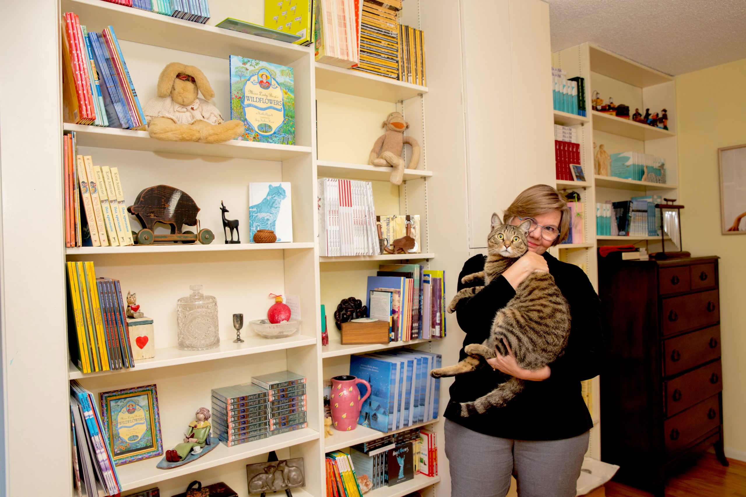 Kathi and Ace pose in front of shelves lined with books authored by Kathi. 