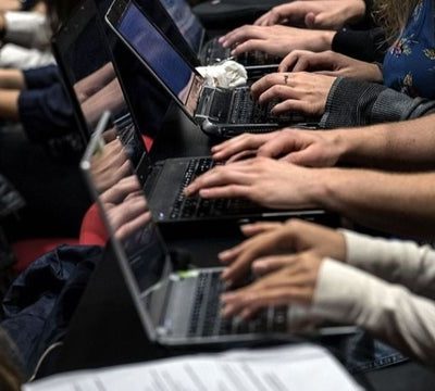 rows of hands typing on laptops in a university classroom