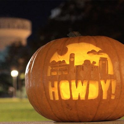 Photo of pumpkin with the campus skyline and the word "Howdy!" carved into it.