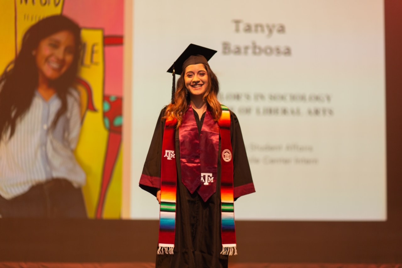 Tanya Barbosa stands proudly in her graduation cap, gown, and other regalia. 