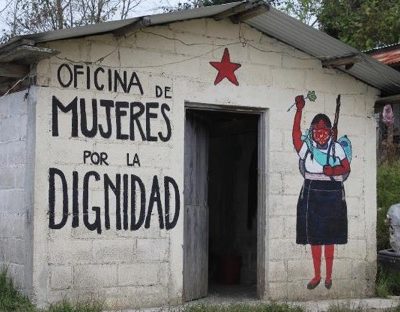 Photo of the Women's Office for Dignity with the building's name painted in Spanish on one side of the door and a women lifting a flower above her head on the other.