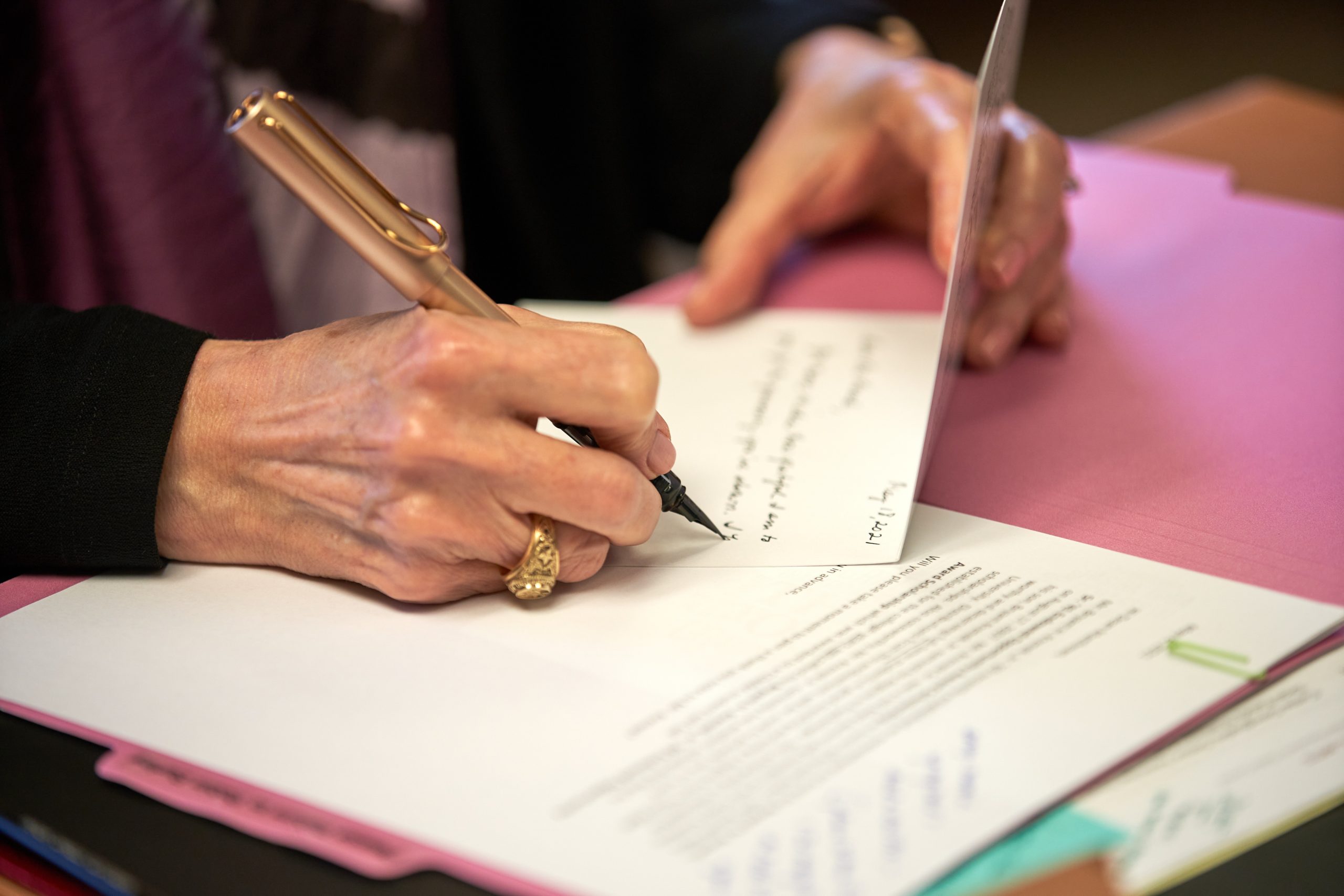 Close up photo of Dean Matthews hands writing a note with a fountain pen. Her Aggie ring is visible as she glides the pen across the page.