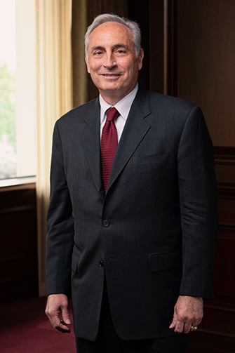 Full length photo of George Harris standing and smiling in a business suite and maroon tie.