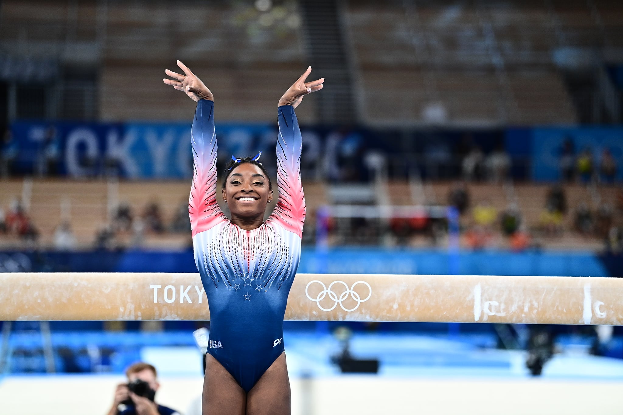 Simone Biles smiles in front of a balance beam. 