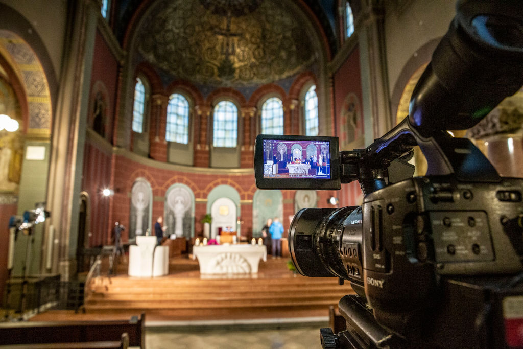A video camera in the foreground is recording a religious service in the blurry background.