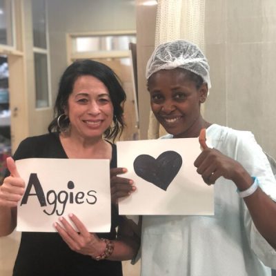 Shawn Andaya-Pulliam poses with a patient while holding a sign that reads "Aggies."