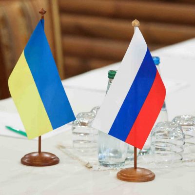 A Ukrainian flag sits beside a Russian flag on a table.