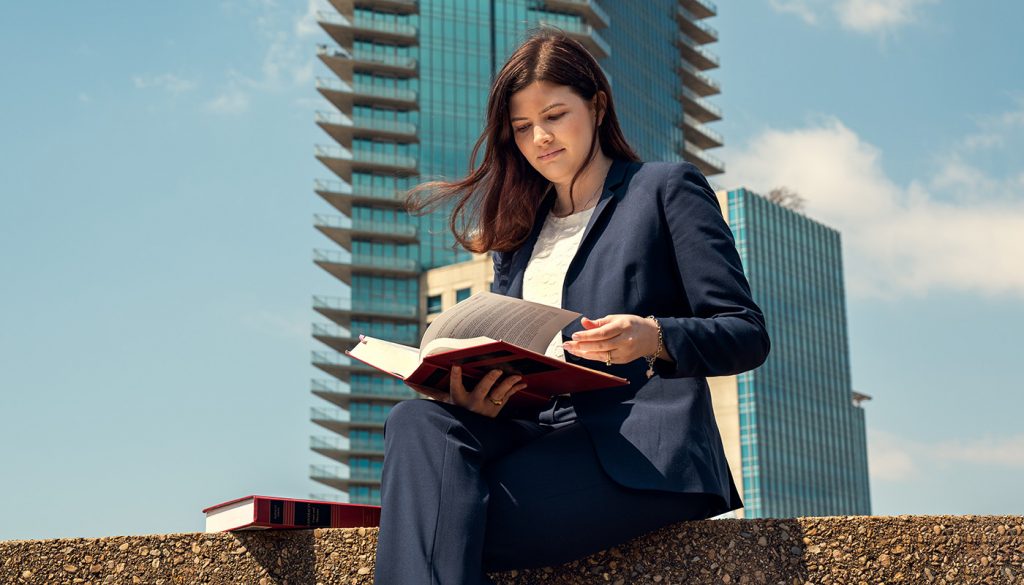 Collier reads a law book while sitting on a ledge with the Dallas skyline behind her.