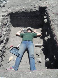 student lays in excavation hole with tools around her